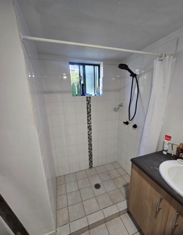Before view of a bathroom shower with white tiles, shower curtain rod and older fixtures