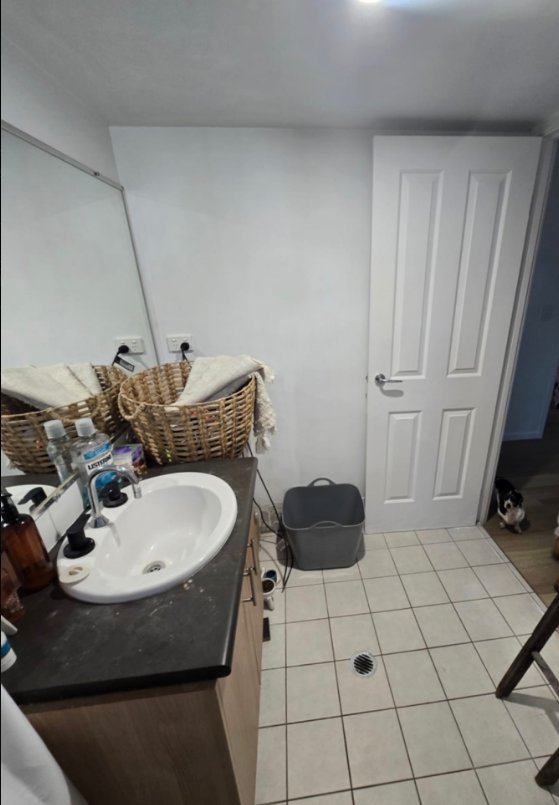 Before view of the same bathroom with older vanity, mirror and tiled floor