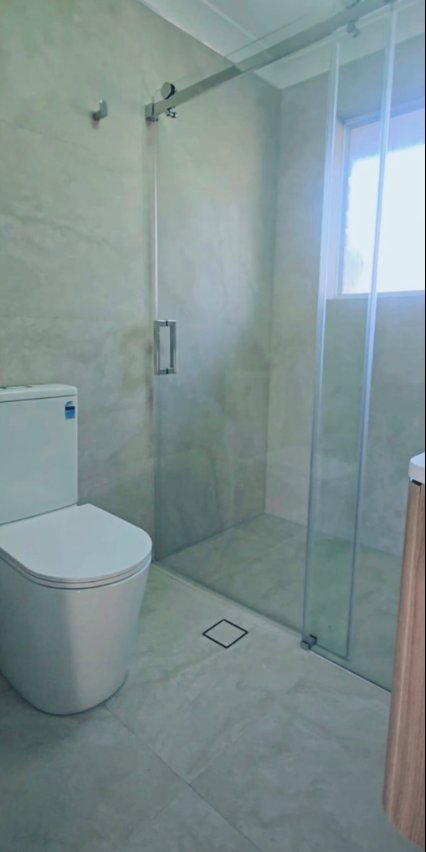 Tiled bathroom with glass shower enclosure, floor waste and white toilet