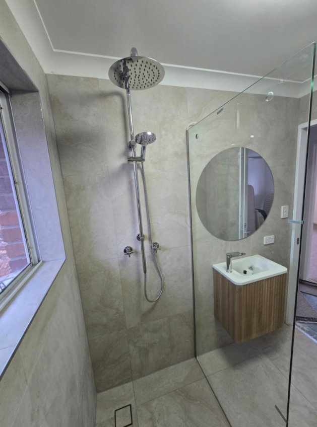 Stone-tiled shower with rain head, glass screen and timber vanity